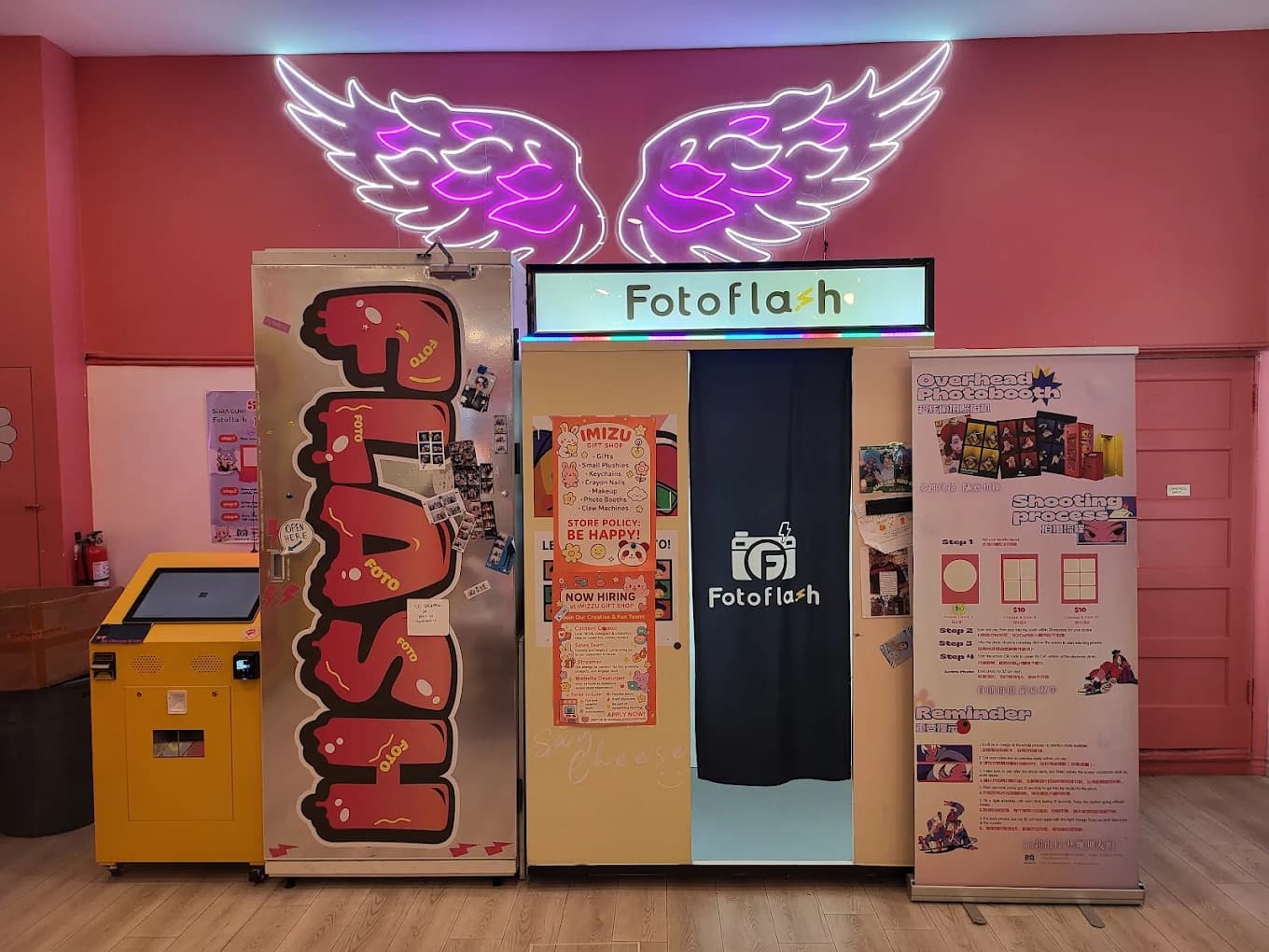 Photobooth in an imizzu shop with a curtain entrance, neon wings, and a yellow kiosk